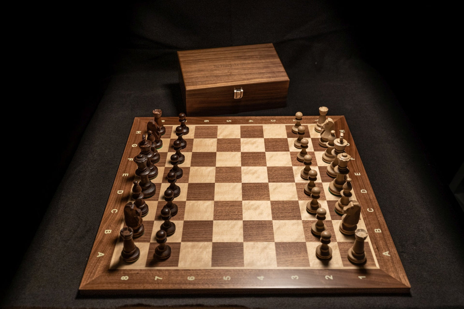 Aufgebautes Schachspiel mit Schachfiguren auf Schachbrett und Aufbewahrungstruhe im Hintergrund