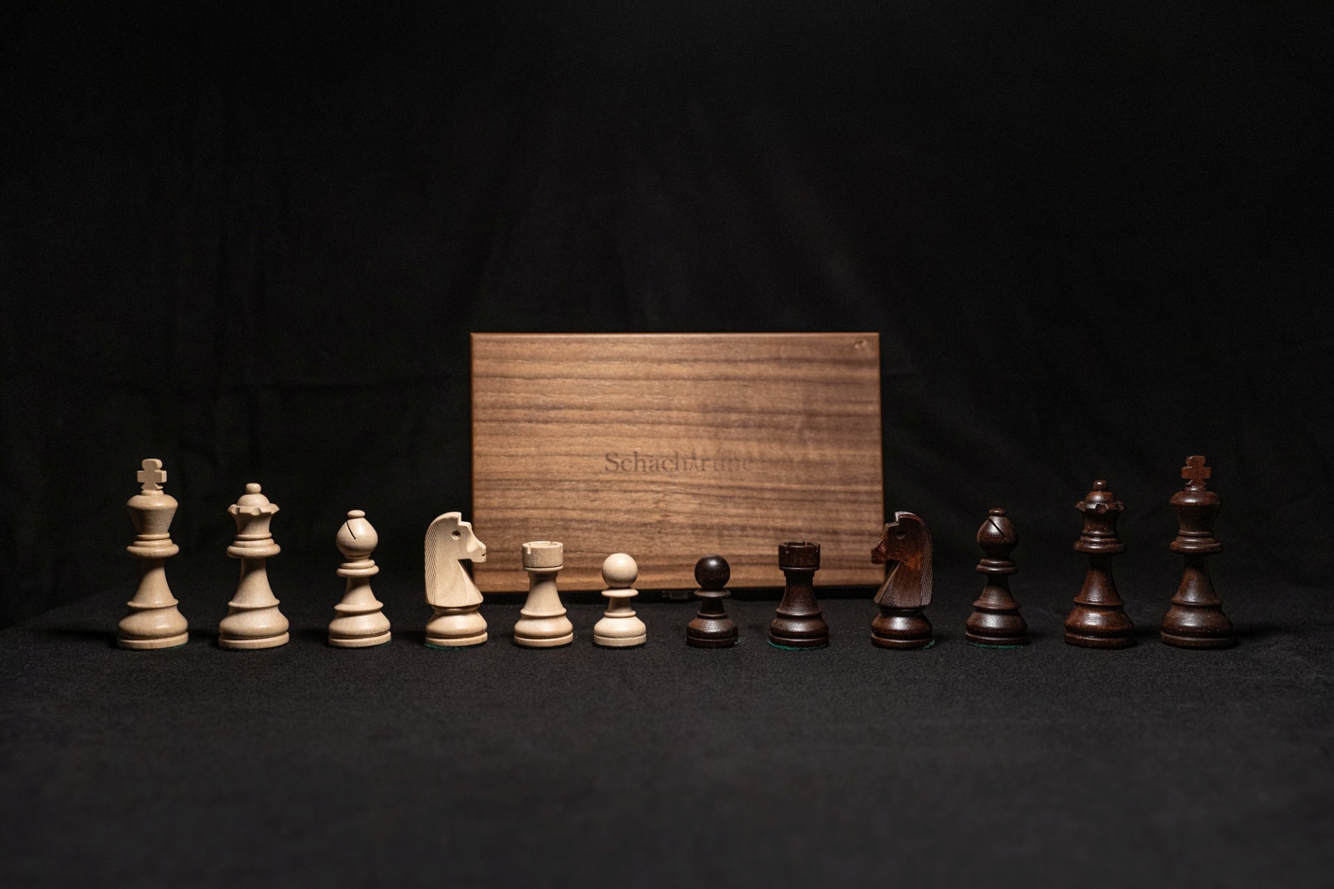 Figurensatz des Schachspiels Manatos aufgereiht mit Aufbewahrungstruhe im Hintergrund