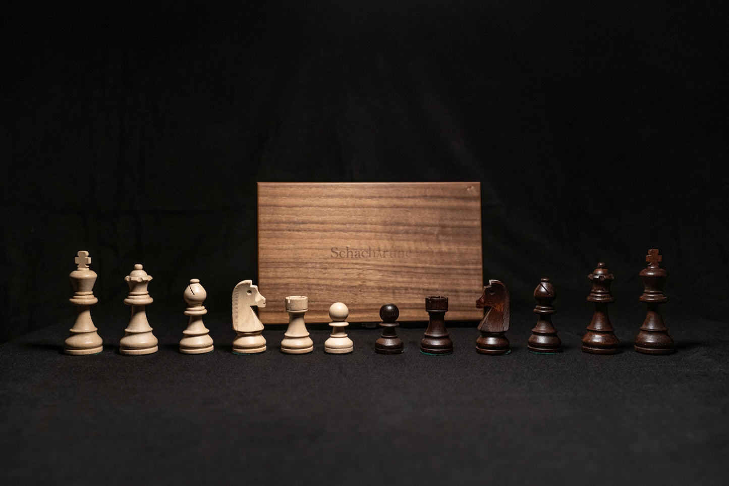 Figurensatz des Schachspiels Torun aufgereiht mit Aufbewahrungstruhe im Hintergrund