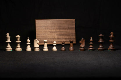 Figurensatz des Schachspiels Calinea aufgereiht mit Aufbewahrungstruhe im Hintergrund