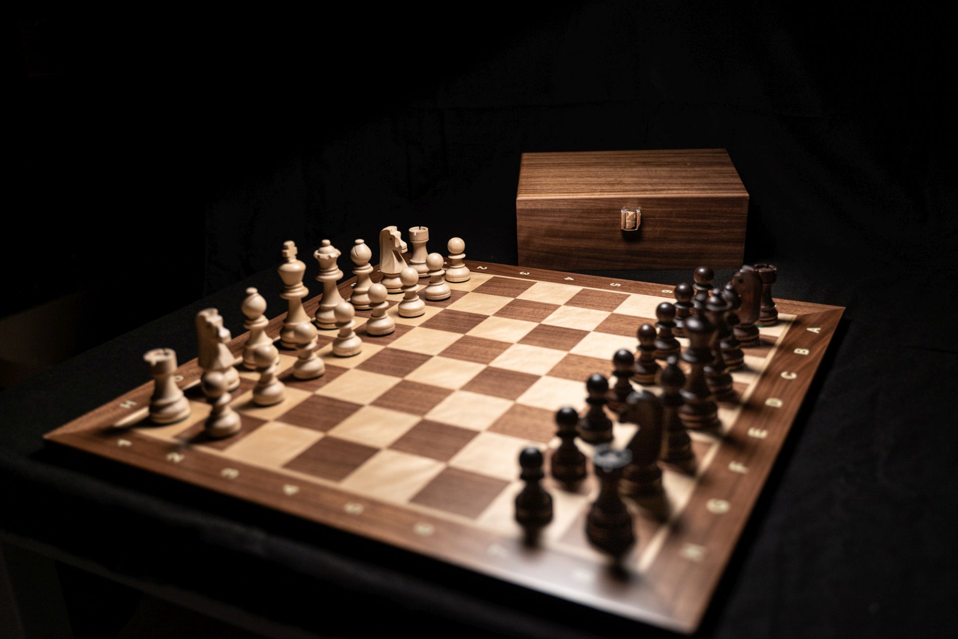 Aufgebautes Schachspiel Manatos mit Aufbewahrungstruhe im Hintergrund